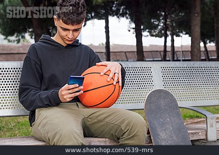 
                Junger Mann, Warten, Sitzbank, Basketball, Smartphone                   